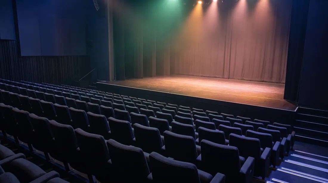 An empty event stage under warm wash lights, with rows of empty seats in front